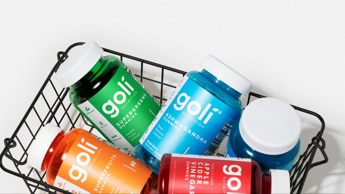 Six bottles of Goli dietary supplements in assorted colors, arranged inside a black wire basket on a clean white background.